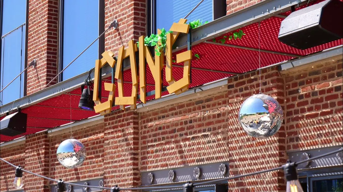 Enseigne en bois GONG accrochée à la façade en briques du bâtiment